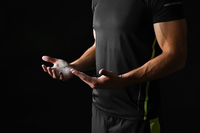 Photo of Man with talcum powder on hands before training against black background, closeup