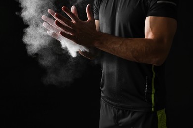 Photo of Man clapping hands with talcum powder before training on black background, closeup