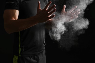 Photo of Man clapping hands with talcum powder before training on black background, closeup