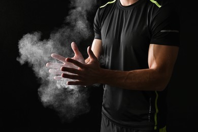 Photo of Man clapping hands with talcum powder before training on black background, closeup