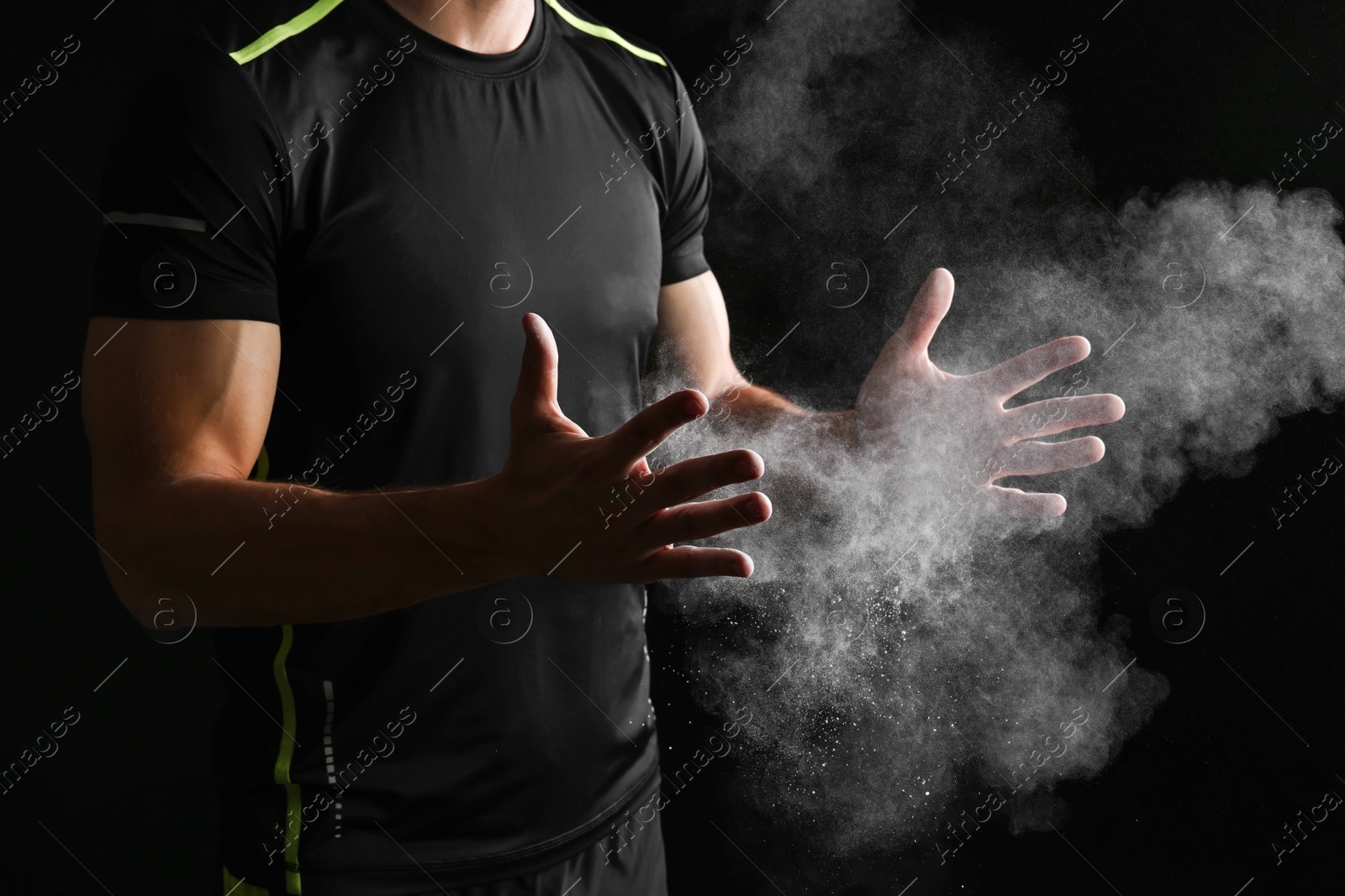 Photo of Man clapping hands with talcum powder before training on black background, closeup