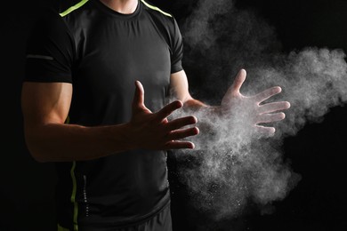 Photo of Man clapping hands with talcum powder before training on black background, closeup