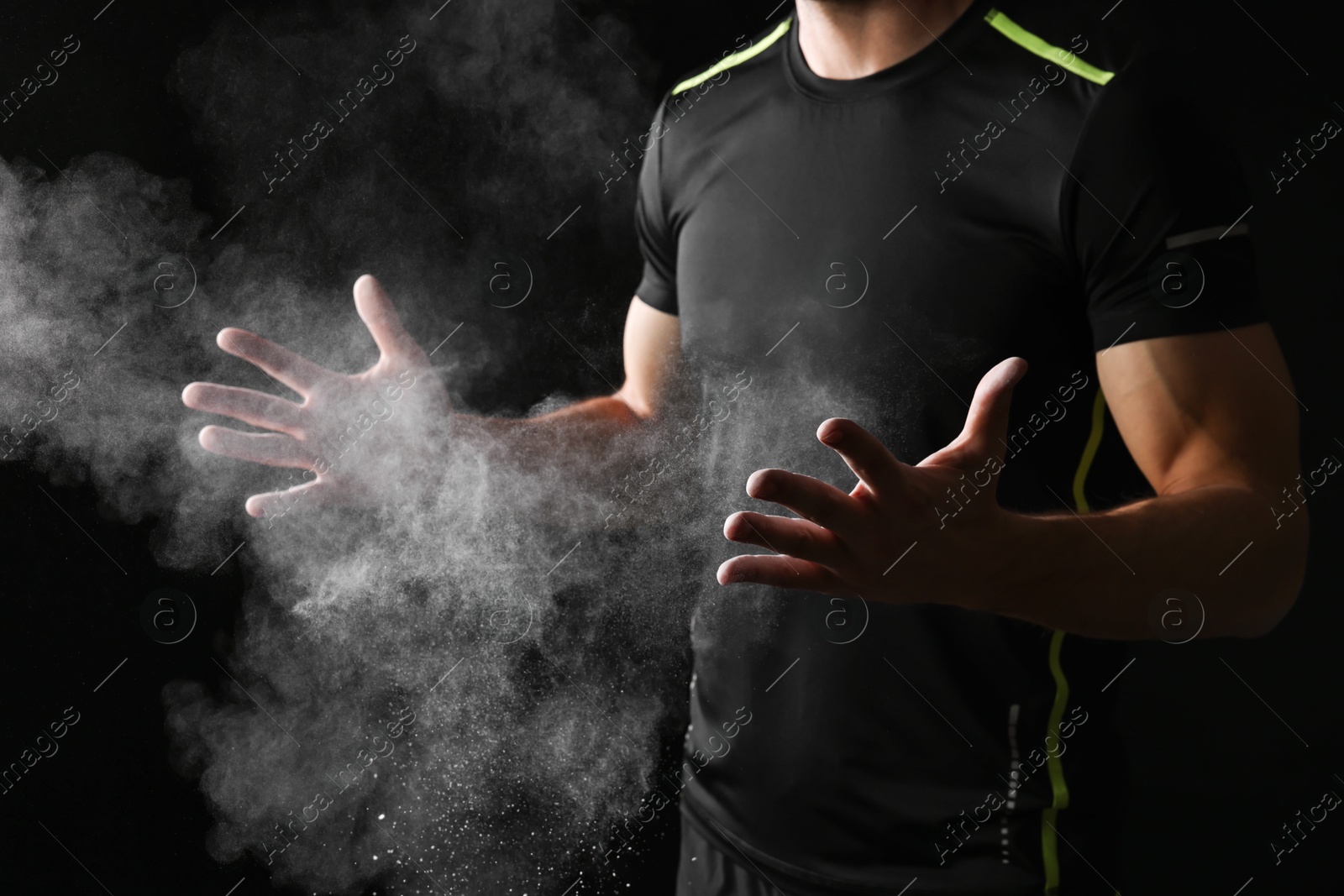 Photo of Man clapping hands with talcum powder before training on black background, closeup