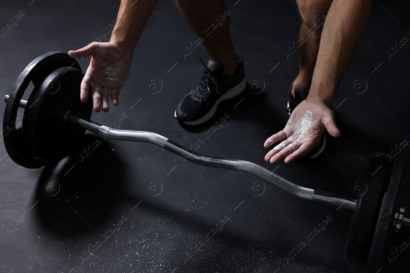 Photo of Man applying talcum powder onto his hands before training with barbell in gym, closeup