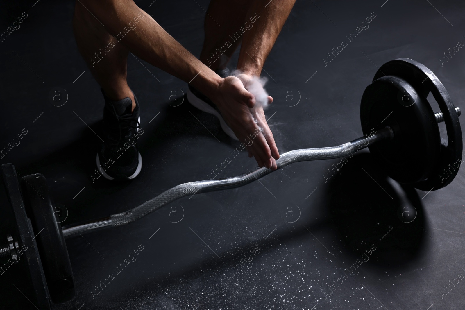 Photo of Man clapping hands with talcum powder before training with barbell in gym, closeup