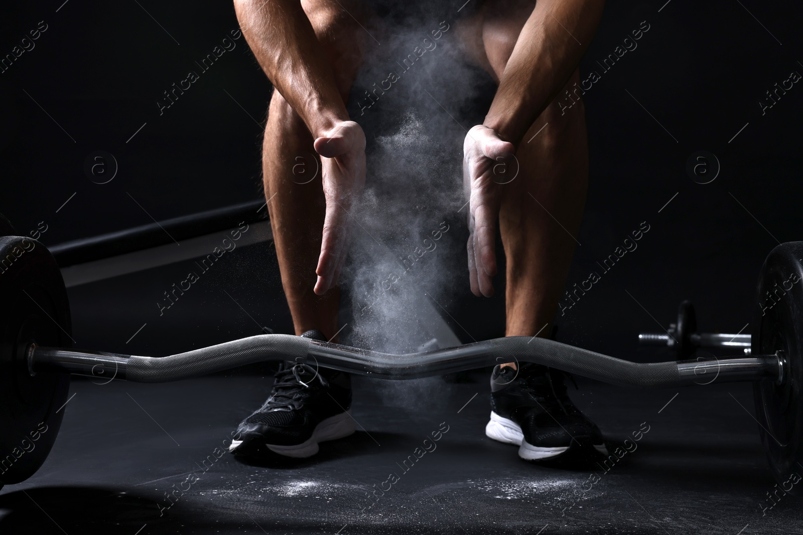 Photo of Man clapping hands with talcum powder before training with barbell in gym, closeup