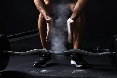 Photo of Man clapping hands with talcum powder before training with barbell in gym, closeup