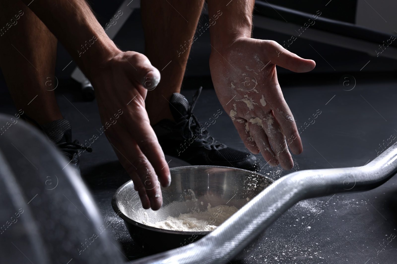 Photo of Man applying talcum powder onto his hands above bowl before training with barbell in gym, closeup