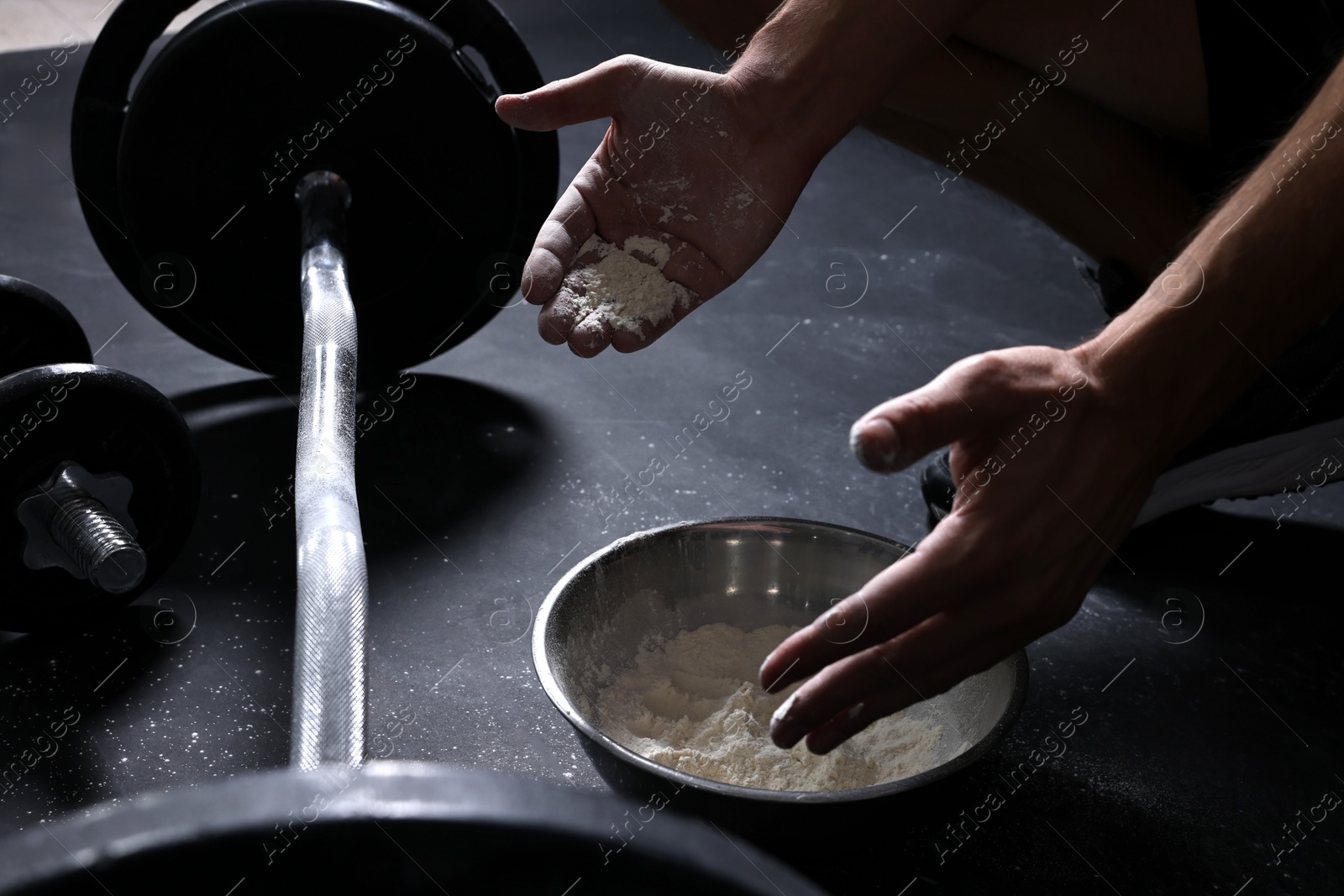 Photo of Man applying talcum powder onto his hands above bowl before training with barbell in gym, closeup