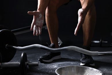 Photo of Man applying talcum powder onto his hands before training with barbell on black background, closeup