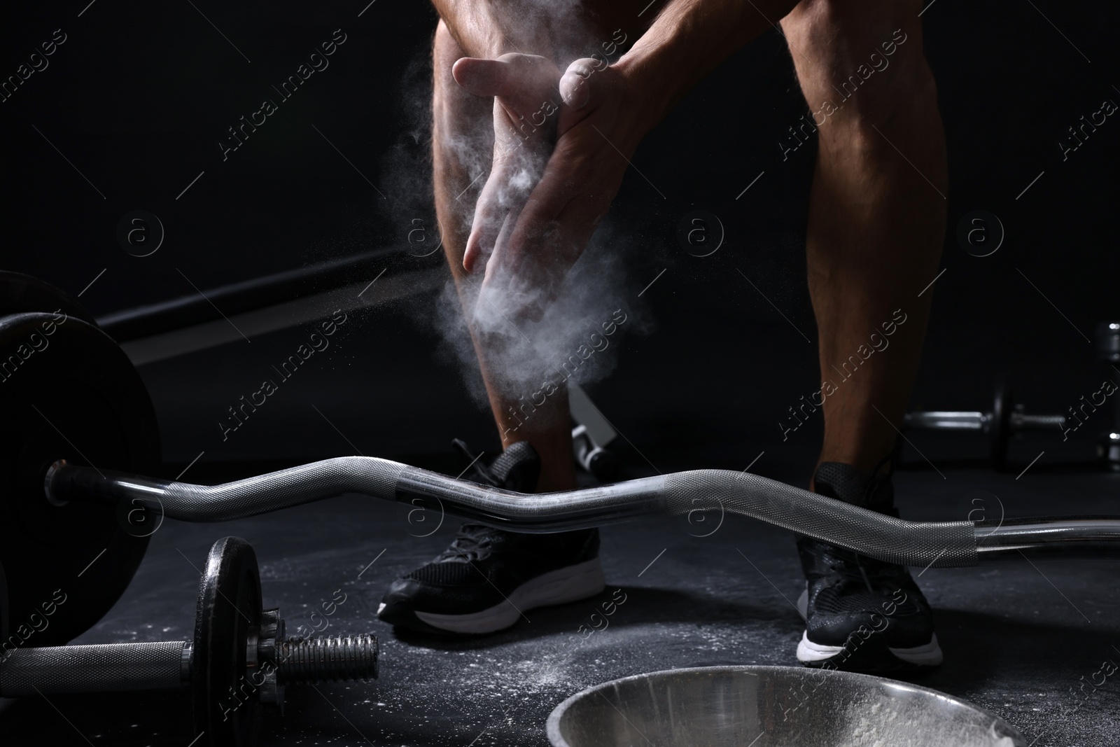 Photo of Man clapping hands with talcum powder before training with barbell on black background, closeup