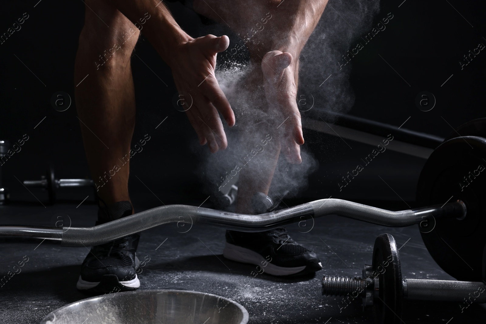 Photo of Man clapping hands with talcum powder before training with barbell on black background, closeup