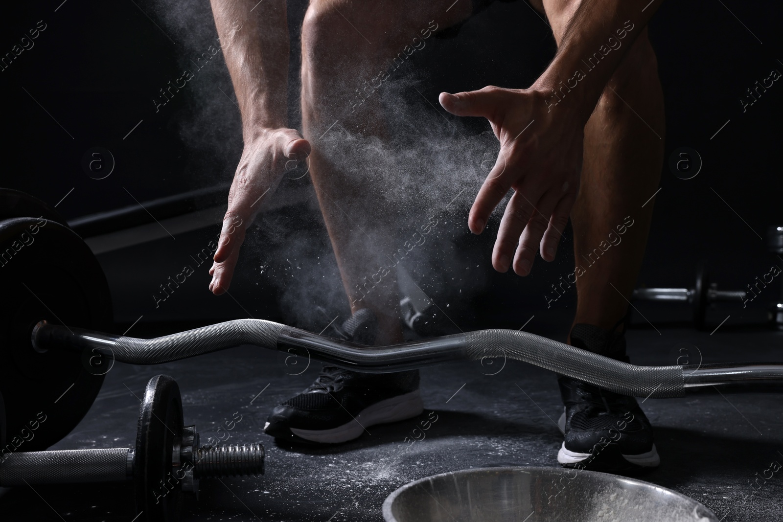 Photo of Man with talcum powder on hands training with barbell against black background, closeup