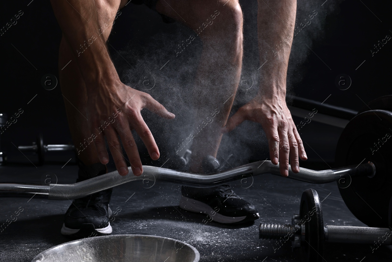 Photo of Man with talcum powder on hands training with barbell against black background, closeup