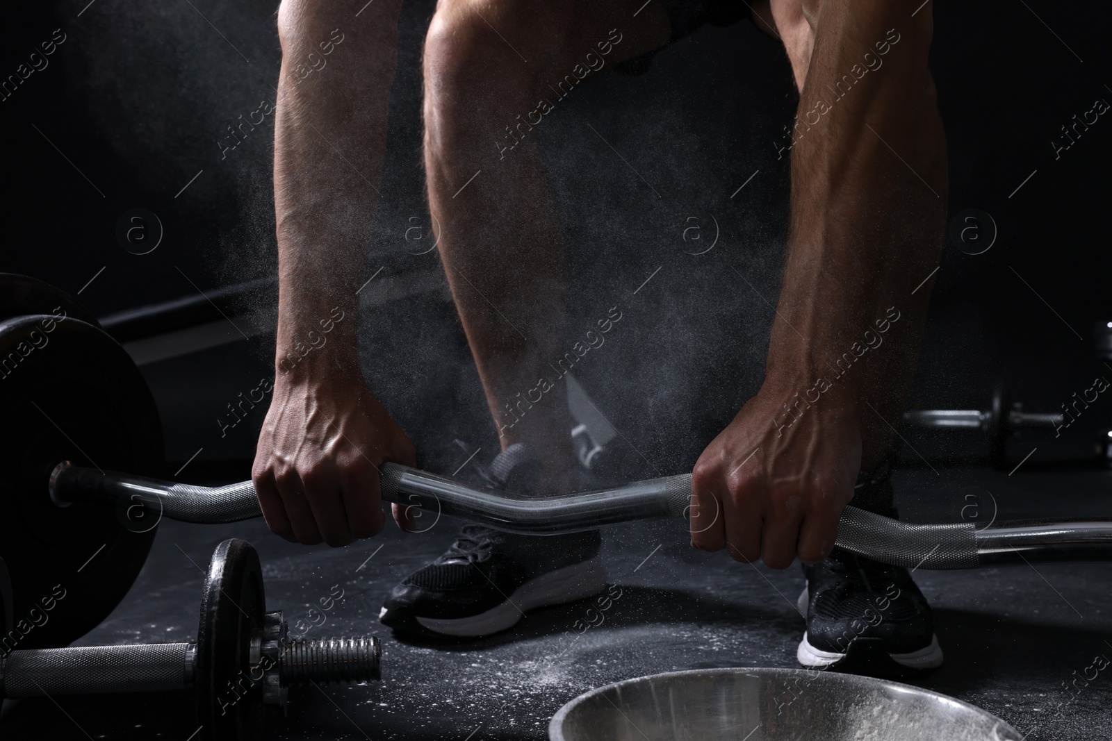 Photo of Man with talcum powder on hands training with barbell against black background, closeup