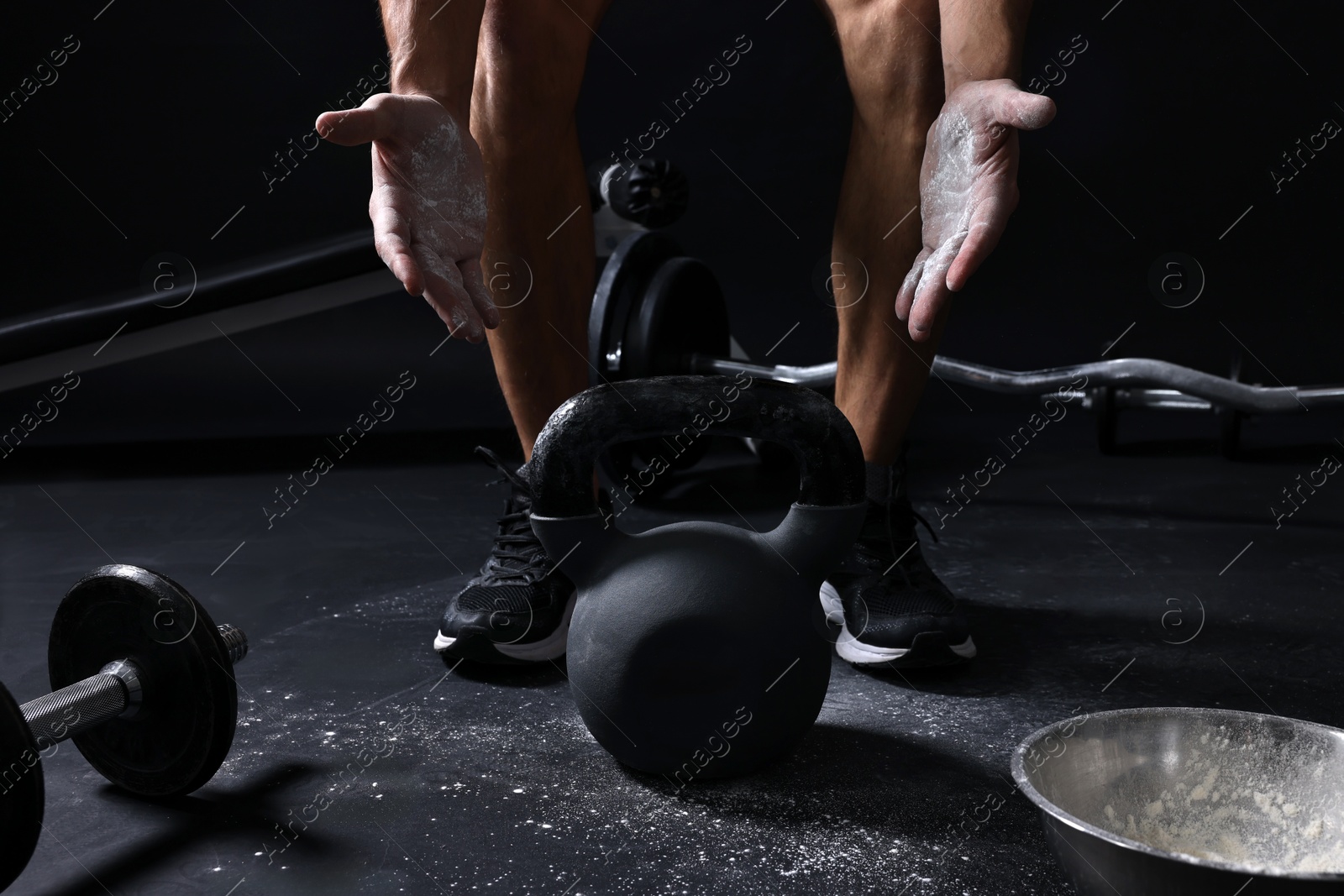 Photo of Man with talcum powder on hands training with kettlebell against black background, closeup