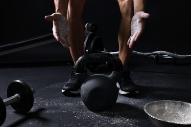 Photo of Man with talcum powder on hands training with kettlebell against black background, closeup