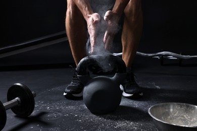 Photo of Man with talcum powder on hands training with kettlebell against black background, closeup