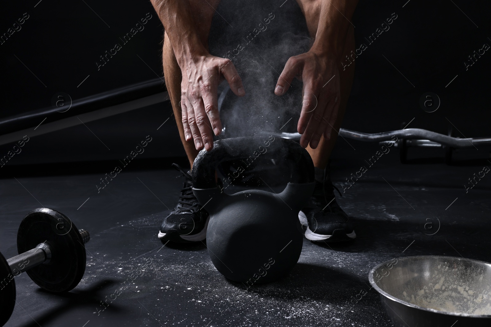 Photo of Man with talcum powder on hands training with kettlebell against black background, closeup