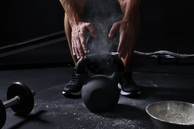 Photo of Man with talcum powder on hands training with kettlebell against black background, closeup