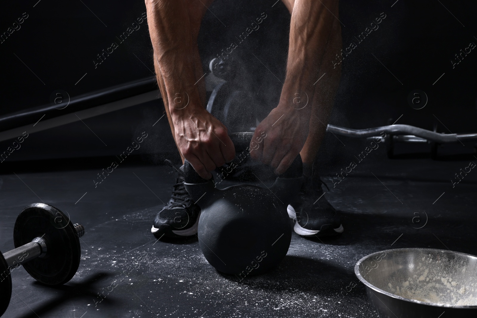 Photo of Man with talcum powder on hands training with kettlebell against black background, closeup