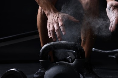 Photo of Man clapping hands with talcum powder before training with kettlebell on black background, closeup