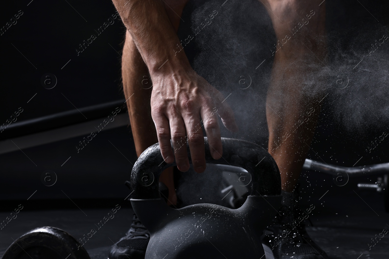 Photo of Man with talcum powder on hands training with kettlebell against black background, closeup