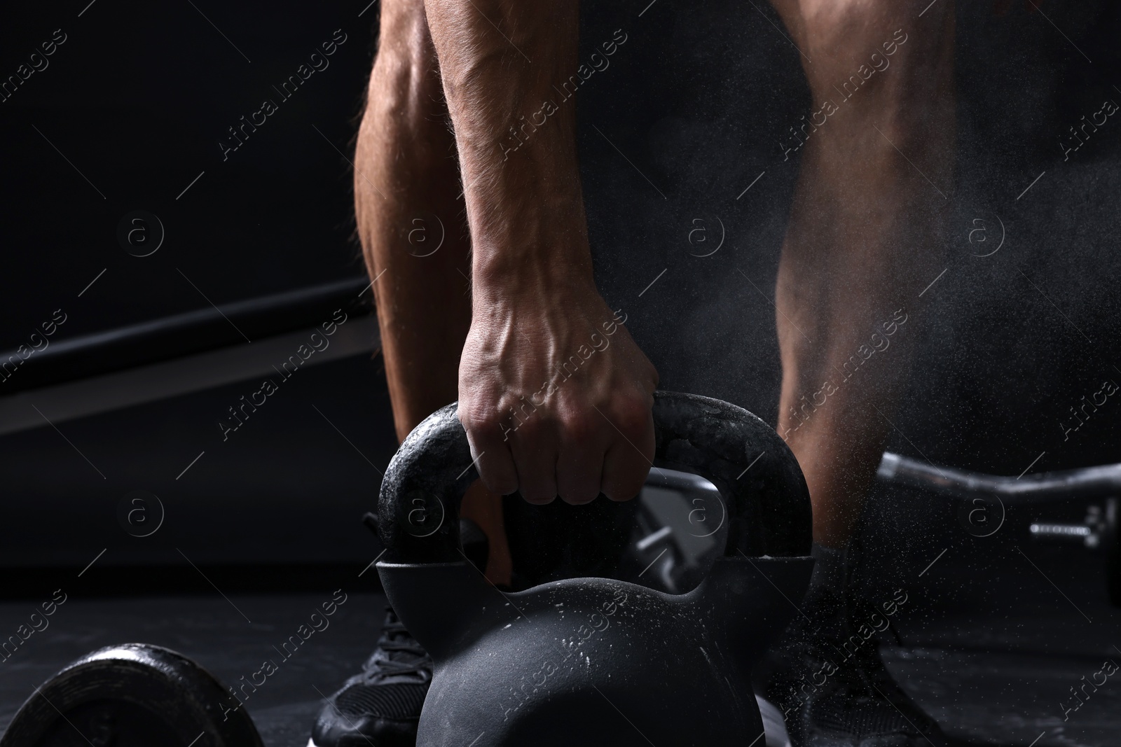 Photo of Man with talcum powder on hands training with kettlebell against black background, closeup