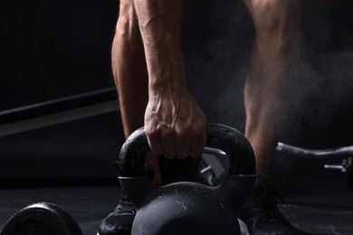 Photo of Man with talcum powder on hands training with kettlebell against black background, closeup