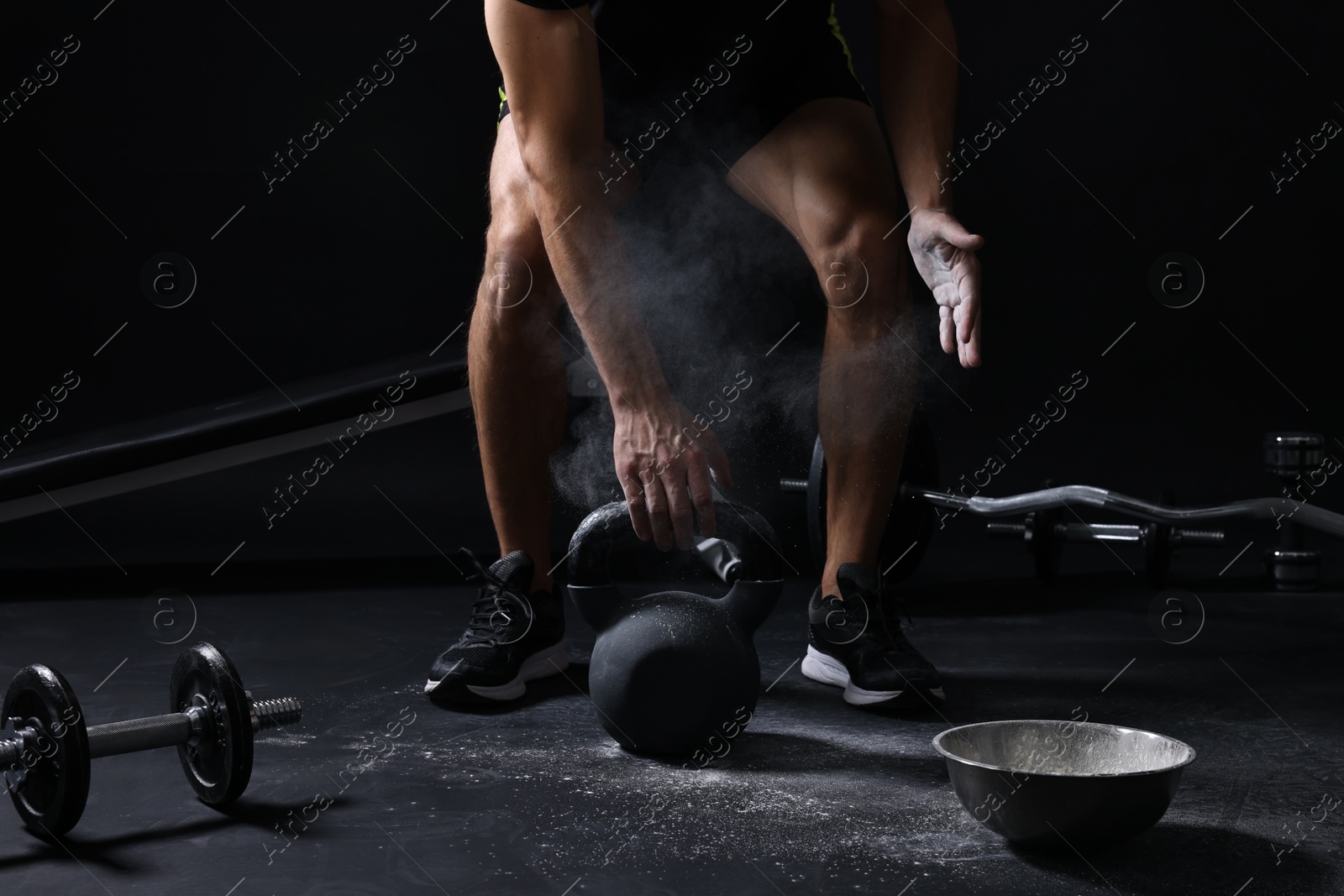 Photo of Man with talcum powder on hands training with kettlebell against black background, closeup