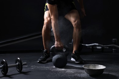 Photo of Man training with kettlebell near bowl of talcum powder on black background, closeup