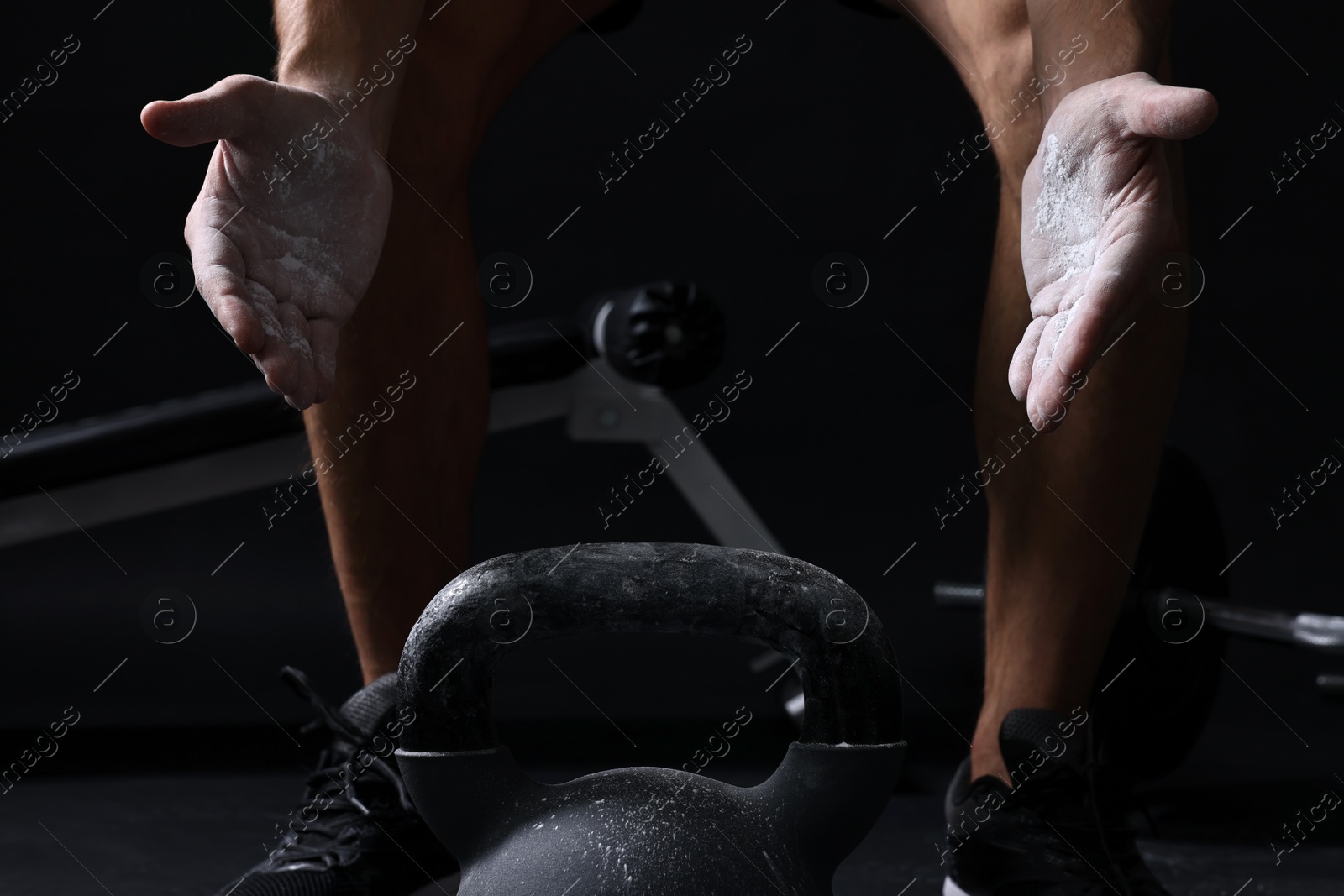 Photo of Man clapping hands with talcum powder before training with kettlebell on black background, closeup