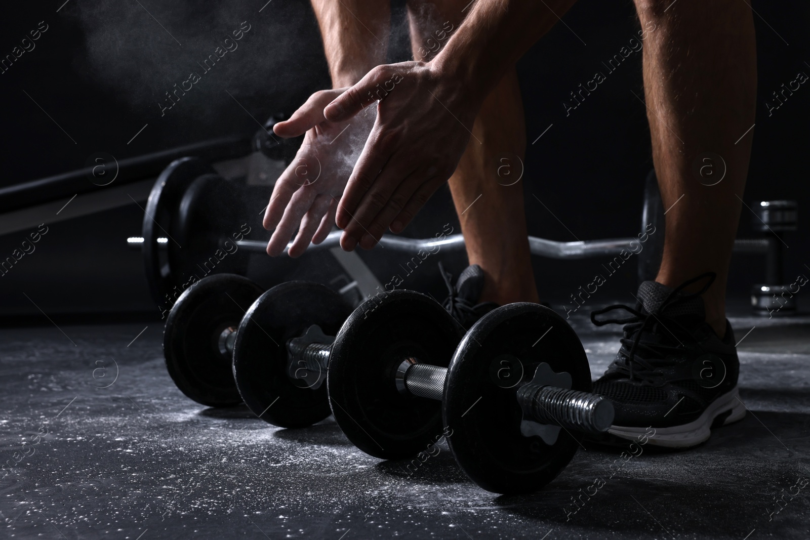 Photo of Man clapping hands with talcum powder before training with barbells on black background, closeup