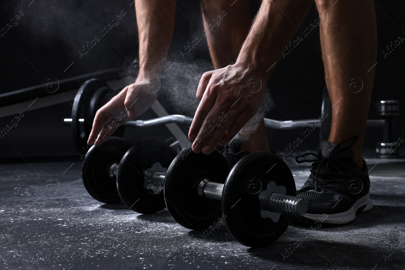 Photo of Man with talcum powder on hands training with barbells against black background, closeup