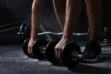 Photo of Man with talcum powder on hands training with barbells against black background, closeup