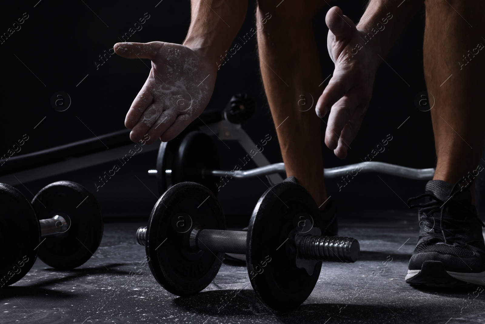 Photo of Man clapping hands with talcum powder before training with barbells on black background, closeup