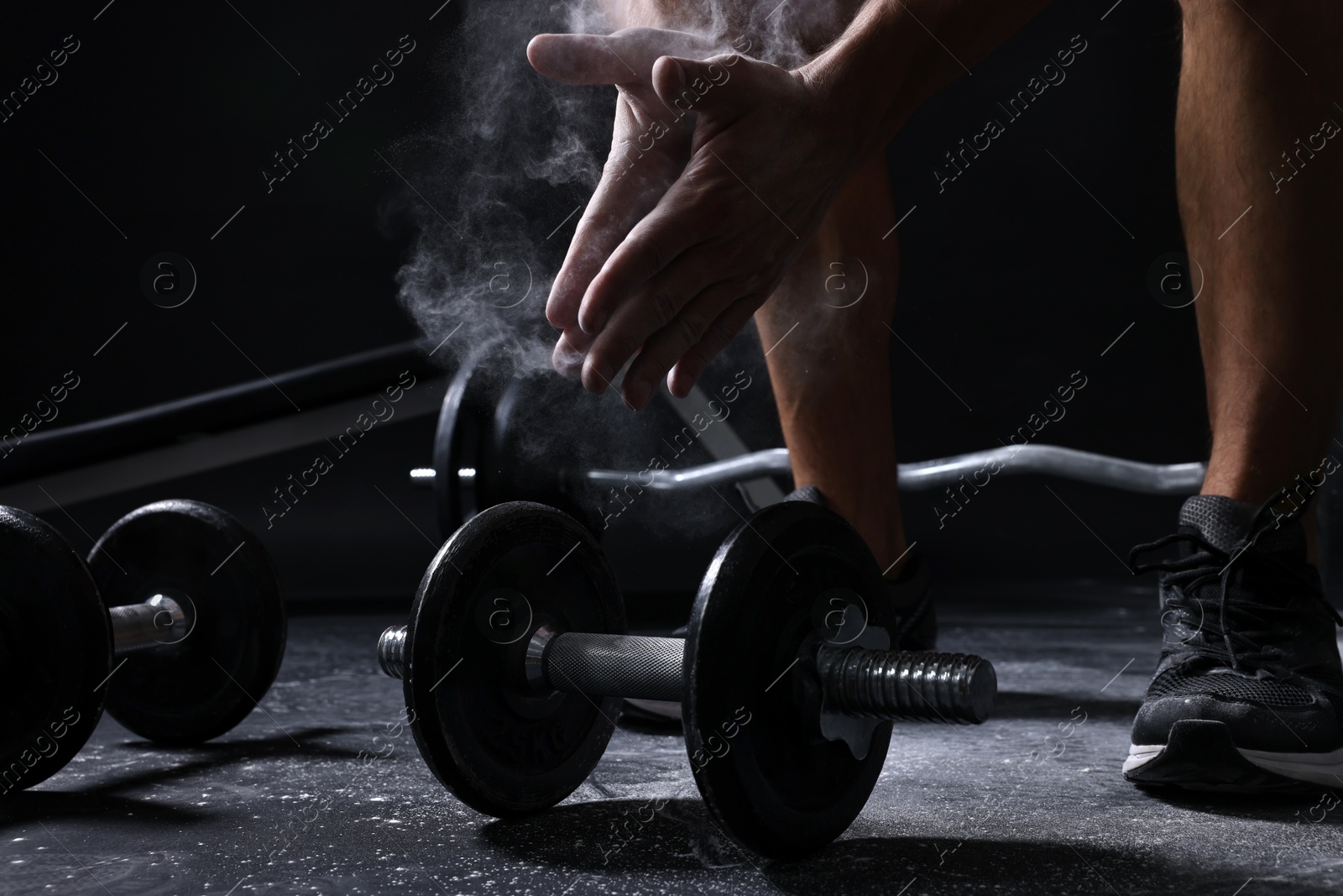 Photo of Man clapping hands with talcum powder before training with barbells on black background, closeup