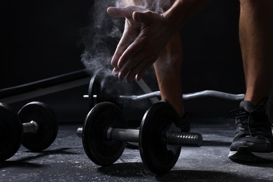 Photo of Man clapping hands with talcum powder before training with barbells on black background, closeup