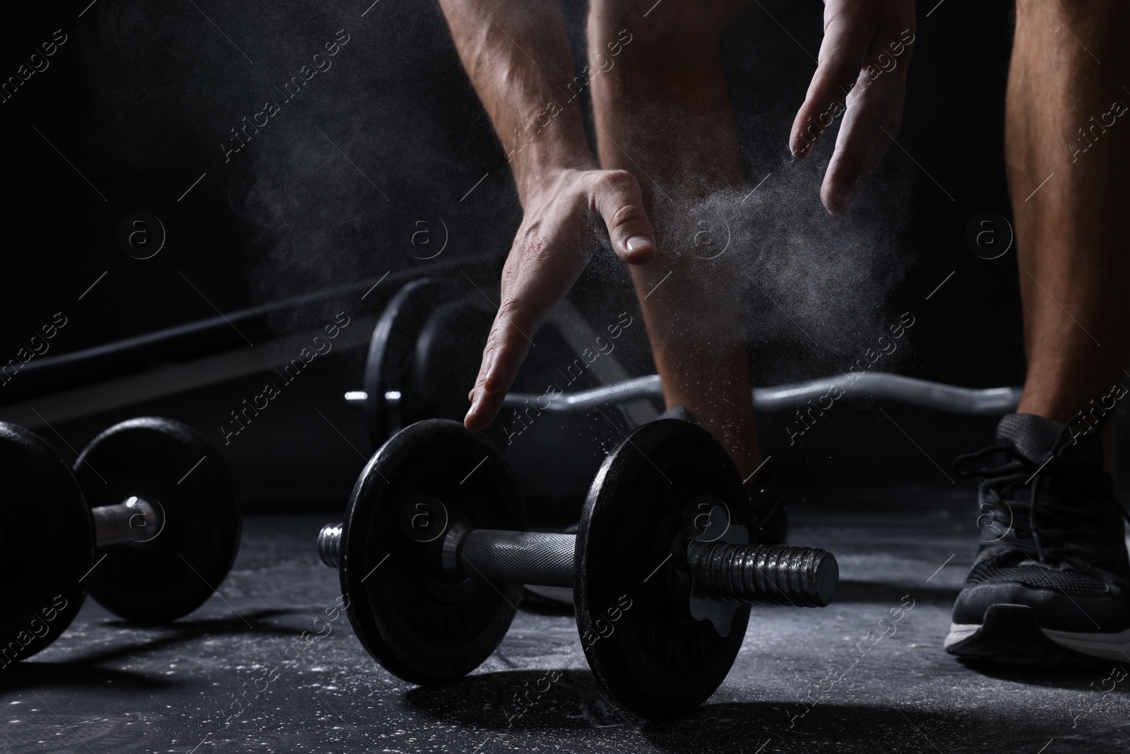 Photo of Man with talcum powder on hands training with barbells against black background, closeup