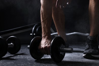 Photo of Man with talcum powder on hands training with barbells against black background, closeup