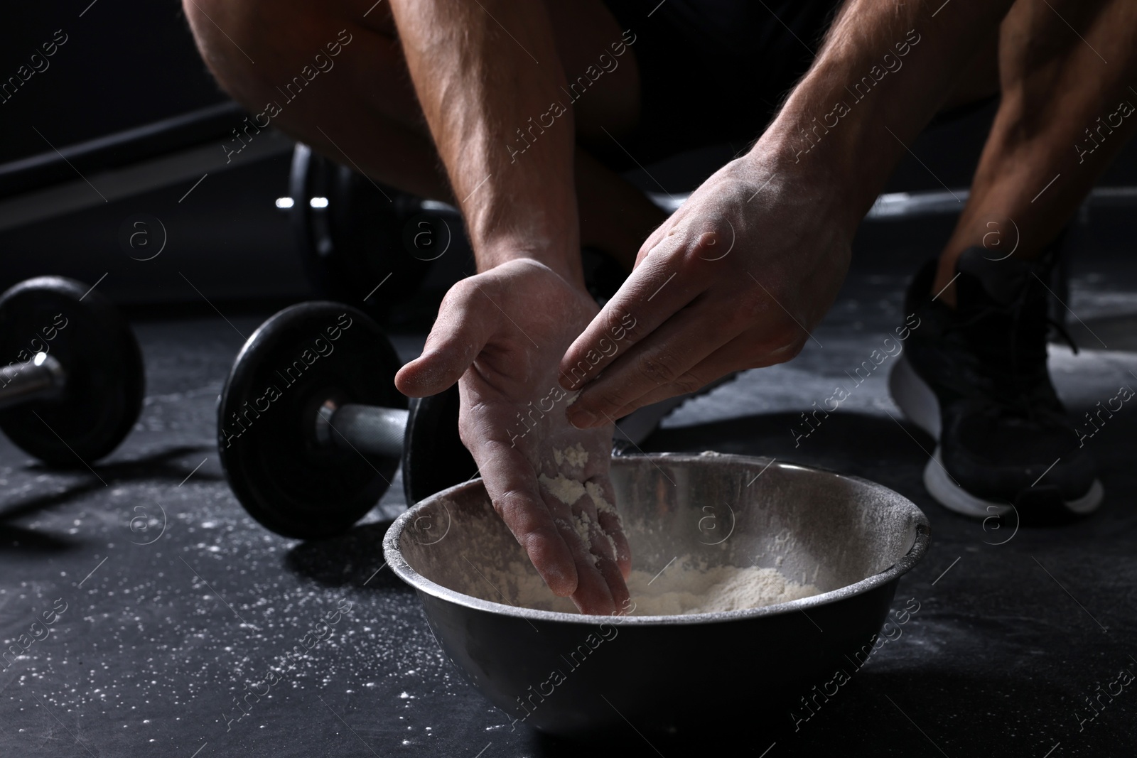 Photo of Man applying talcum powder onto his hands above bowl before training in gym, closeup