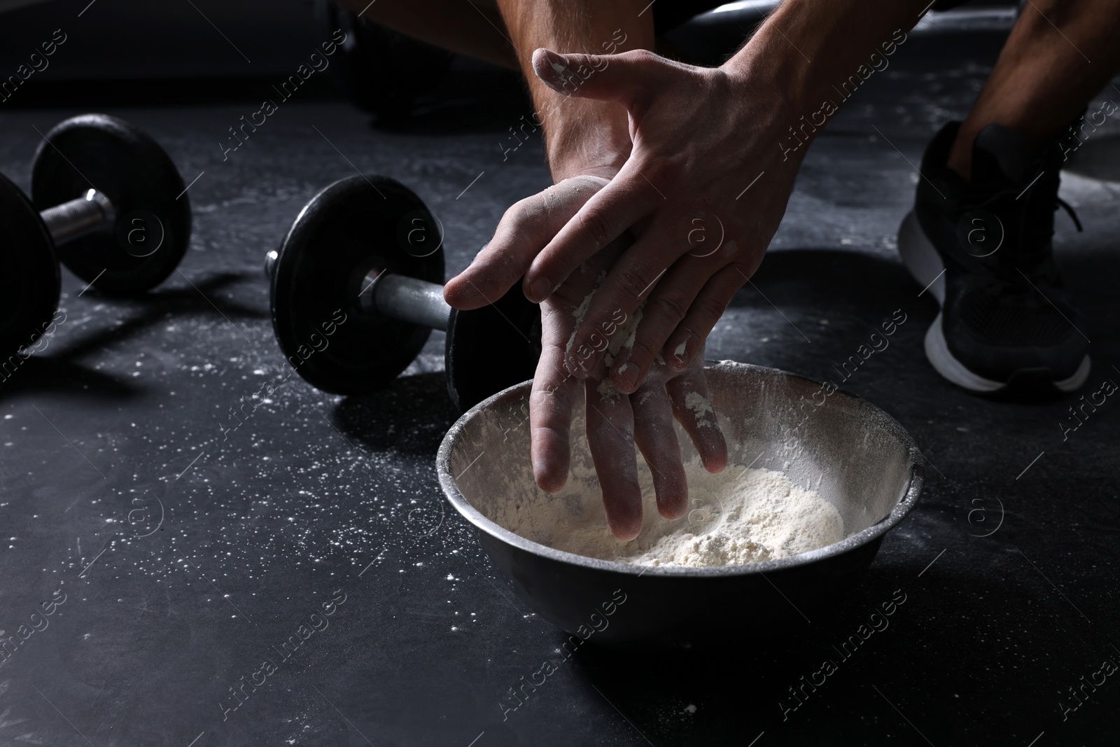 Photo of Man applying talcum powder onto his hands above bowl before training in gym, closeup