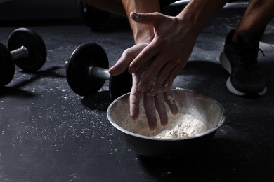 Photo of Man applying talcum powder onto his hands above bowl before training in gym, closeup