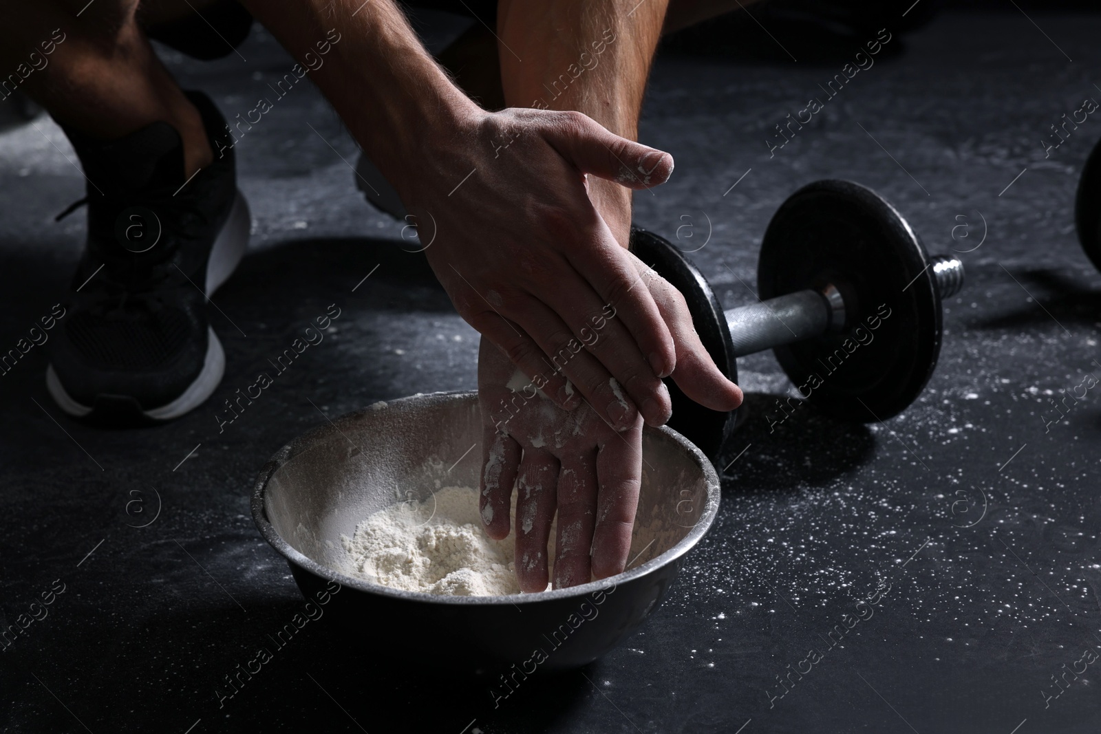 Photo of Man applying talcum powder onto his hands above bowl before training in gym, closeup