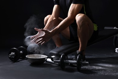 Photo of Man clapping hands with talcum powder above bowl before training on black background, closeup