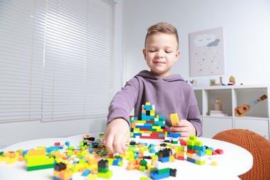 Photo of Cute boy playing with building blocks at white table indoors. Space for text