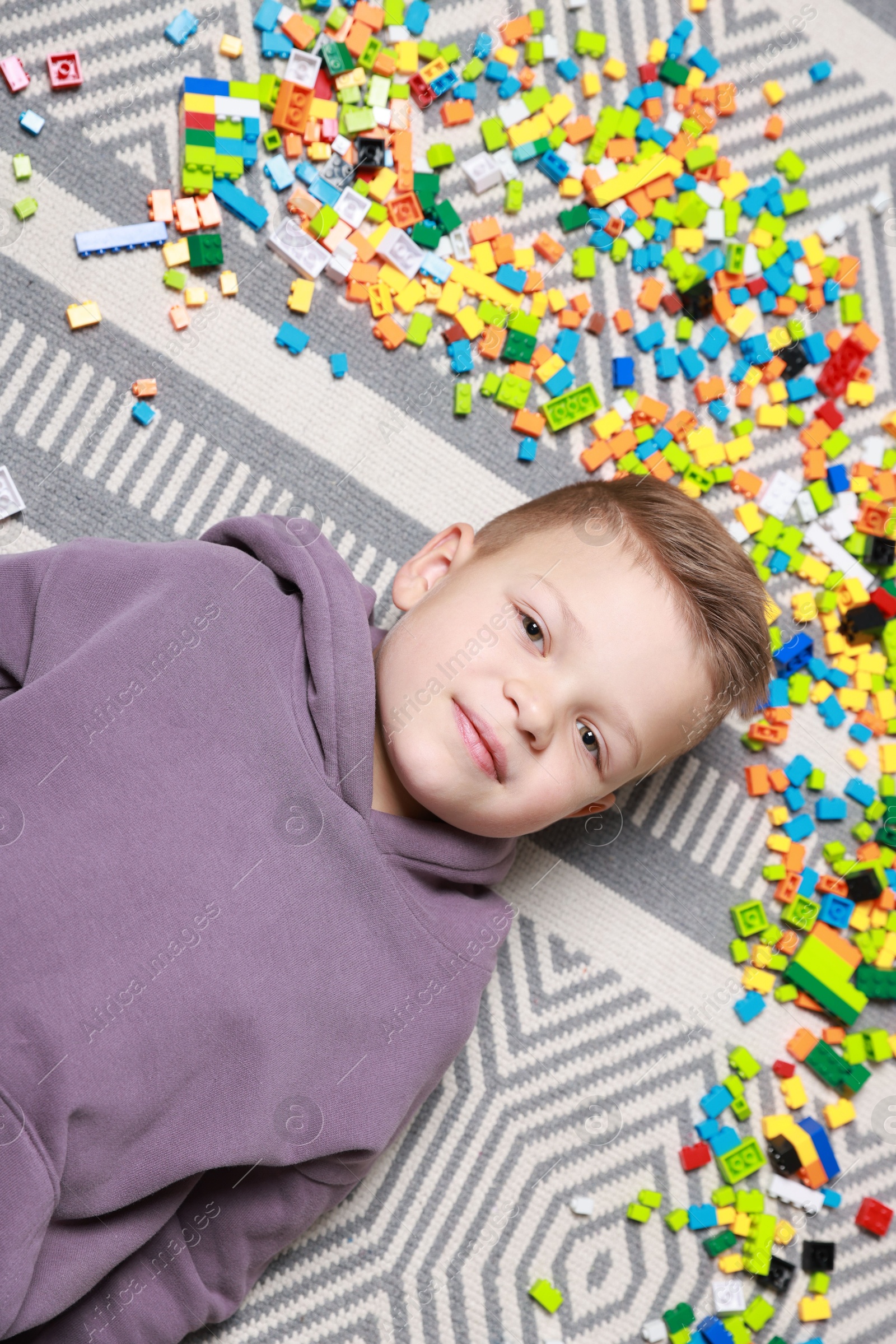 Photo of Cute boy and colorful building blocks on floor, top view