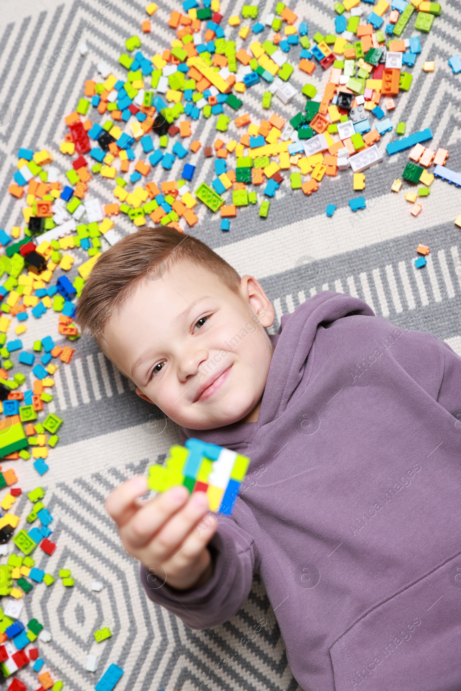 Photo of Cute boy and colorful building blocks on floor, top view