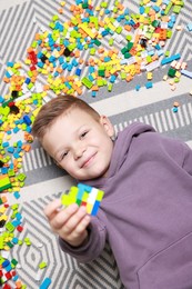 Photo of Cute boy and colorful building blocks on floor, top view