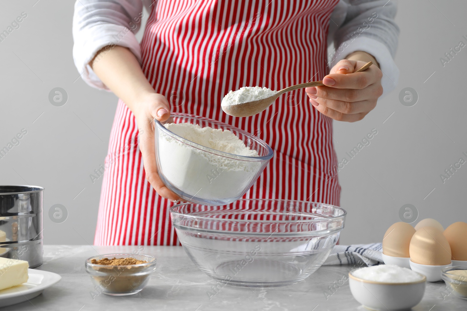 Photo of Making cinnamon rolls. Woman adding flour into bowl at gray marble table, closeup